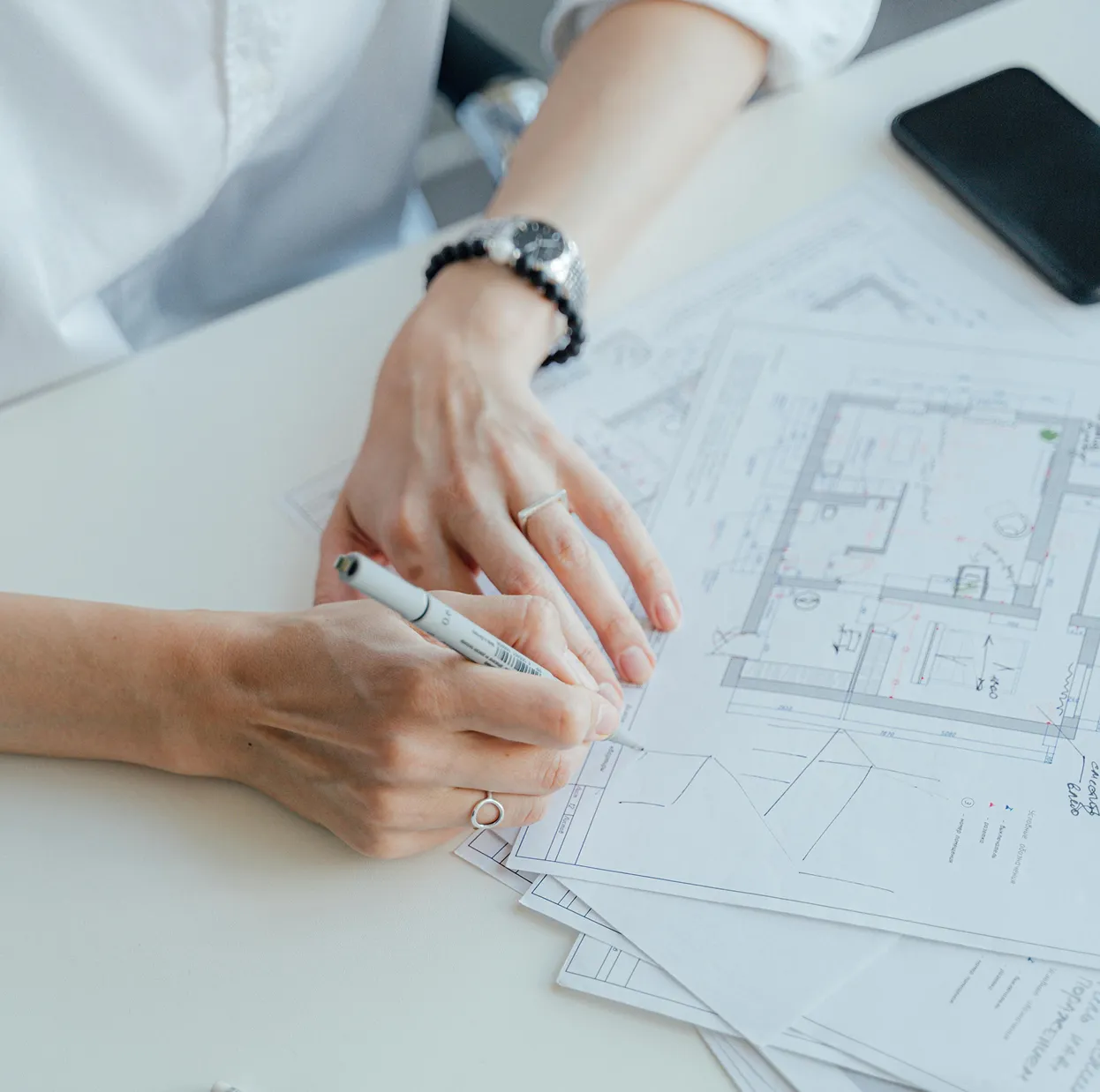 Person sketching and taking notes on architectural blueprints at a desk.