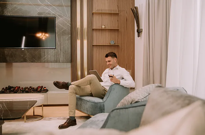 Man relaxing on a sofa in a modern living room, holding a smartphone and working on a tablet.